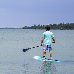 A man paddle boarding on a beach using Pulse The Summy 11' Rectech Board
