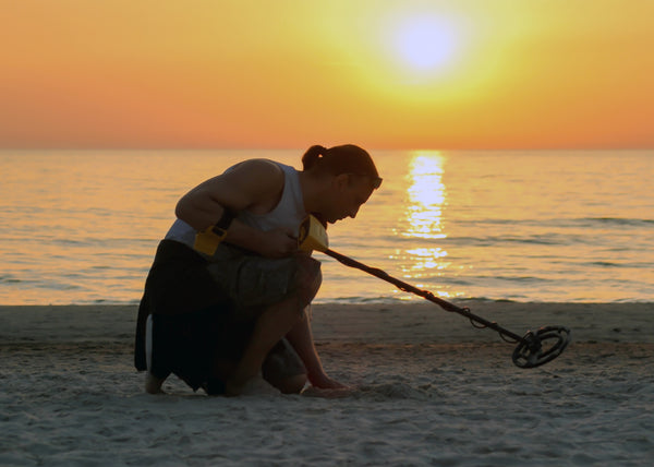 Woman with a metal detector, sun setting. 