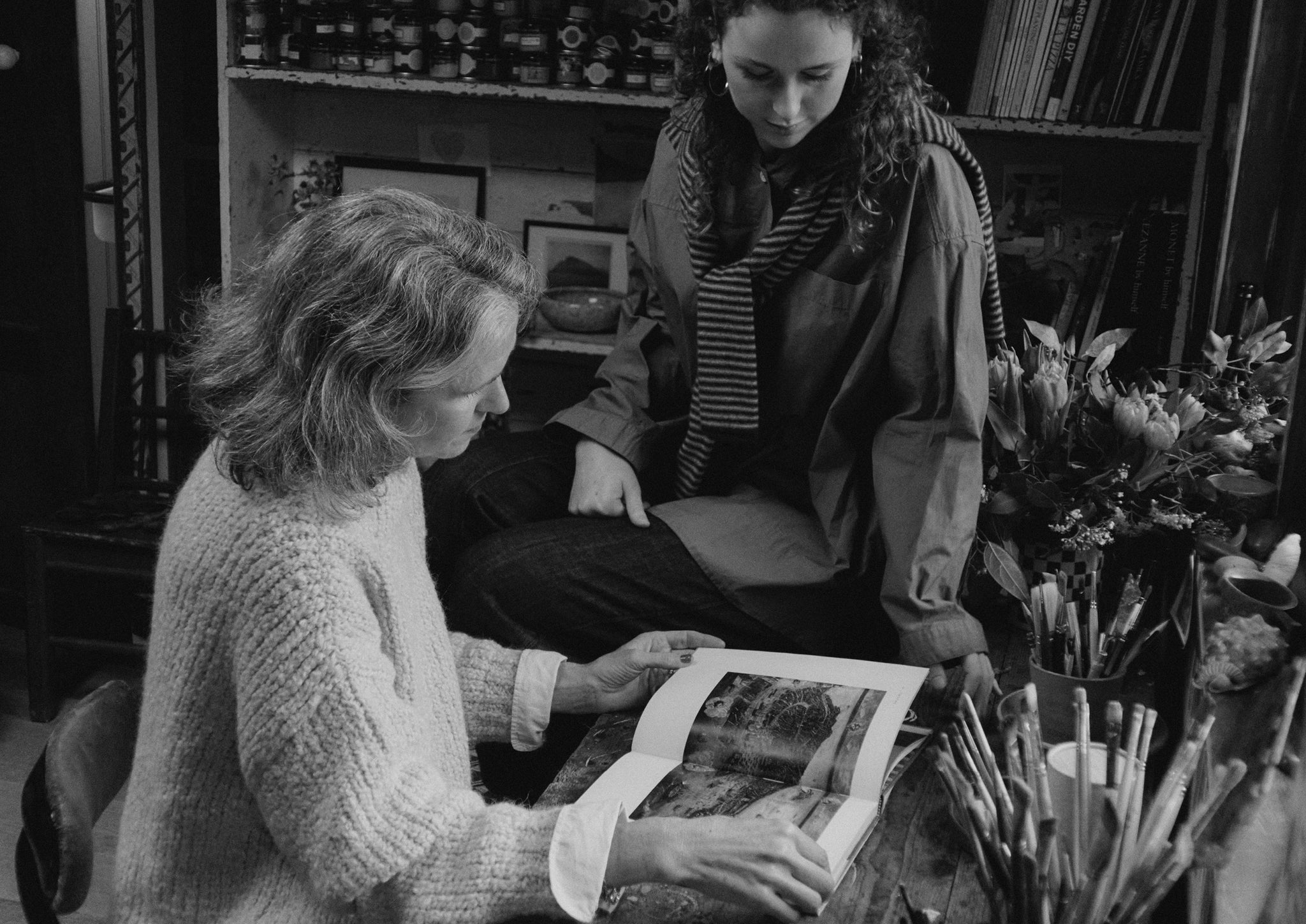 Two women studying a book by a desk.