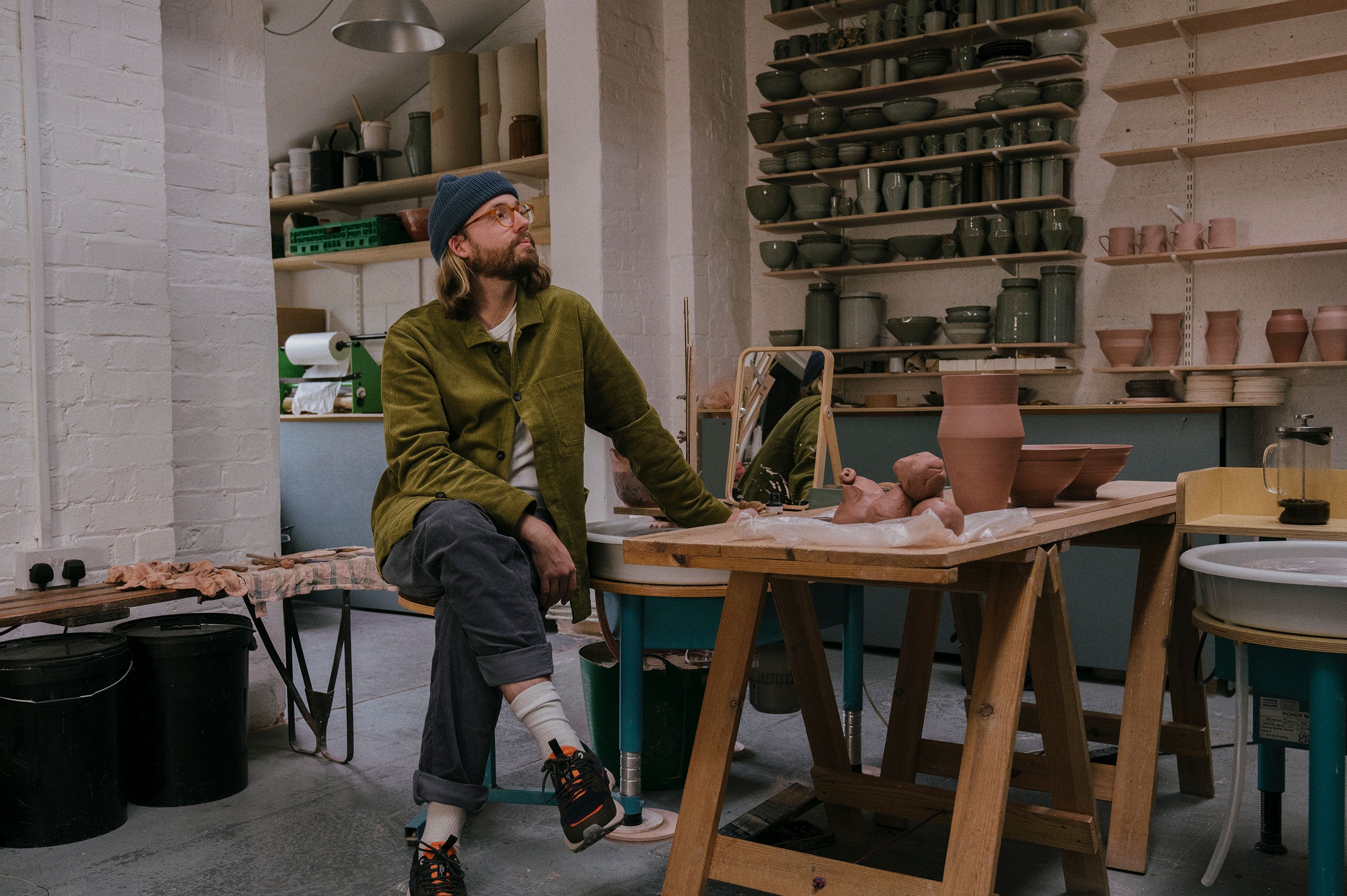 Man in green jacket sat in pottery studio