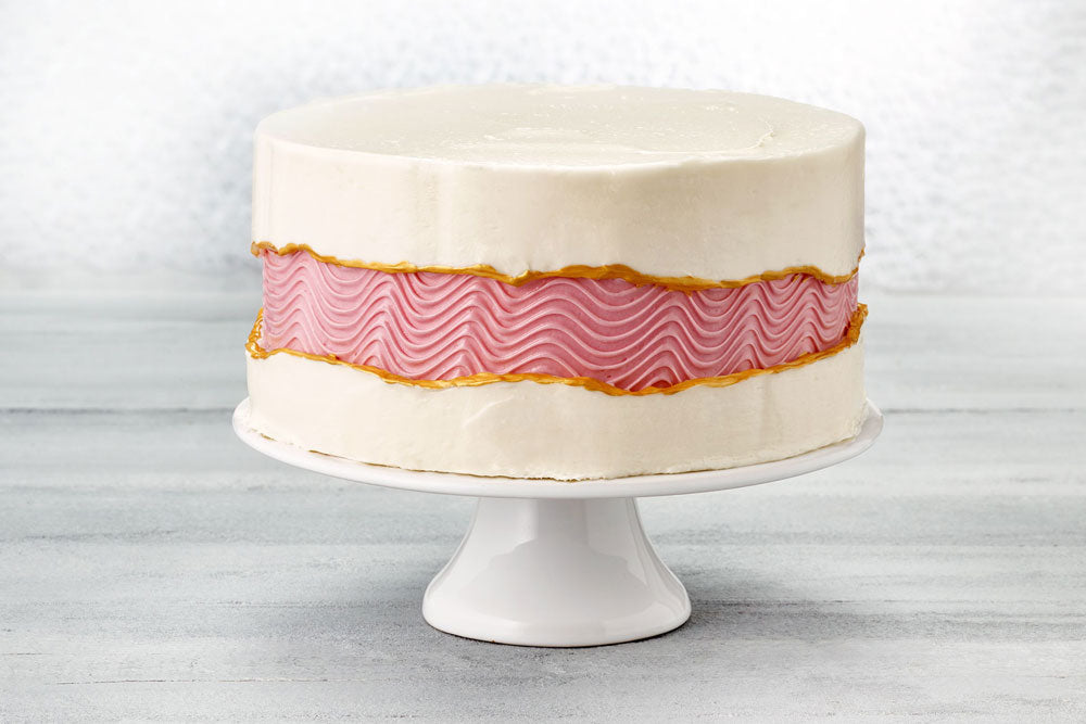 A white cake against a gray backdrop with a wavy pink stripe across the center. 