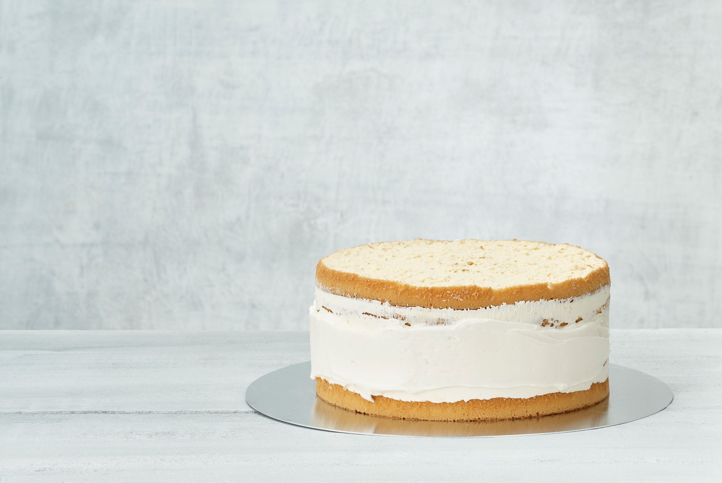 A vanilla cake against a white backdrop with a buttercream crumb coat across the center. 