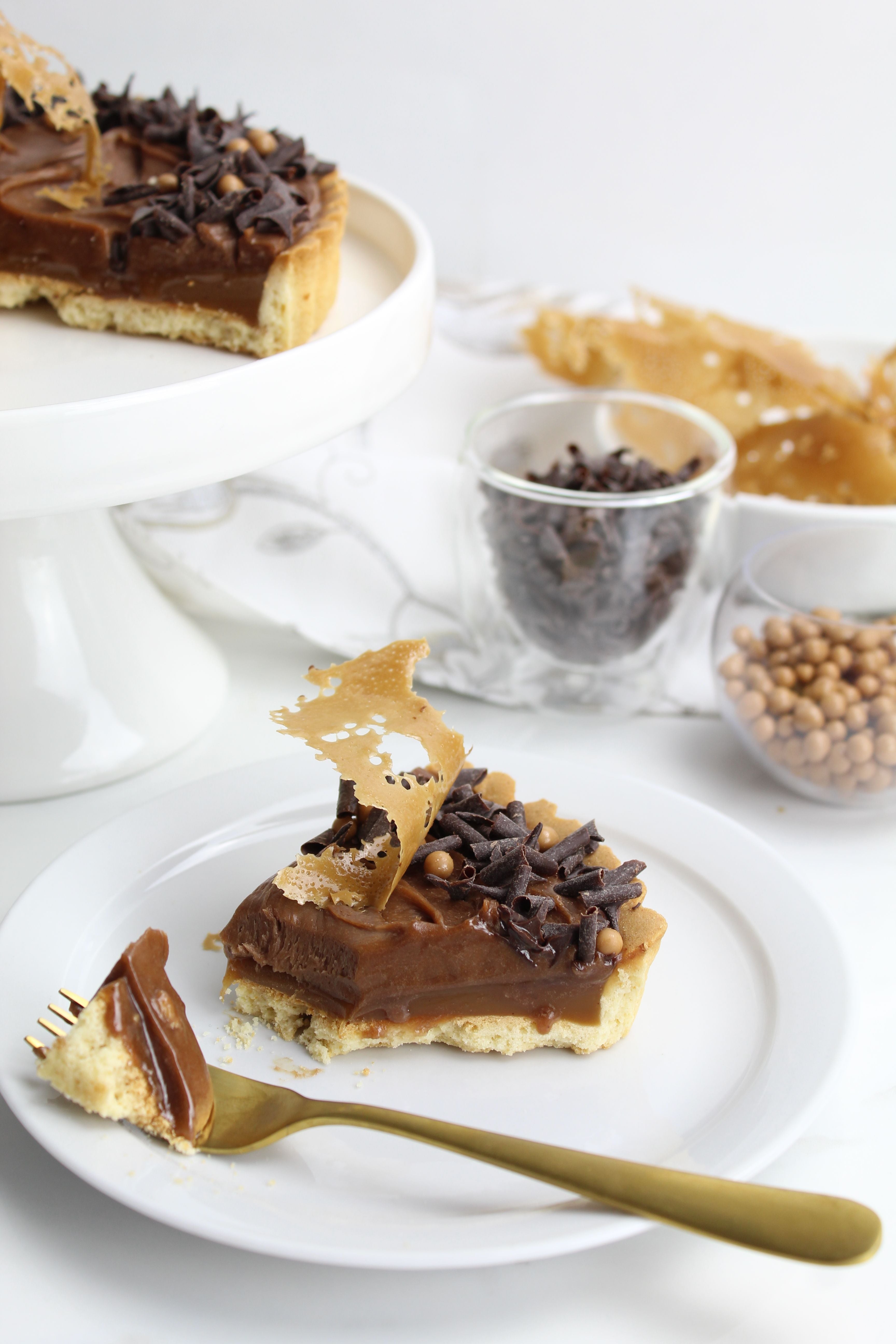 Slice of Chocolate Caramel Twix Tart on a plate with assorted chocolate toppings