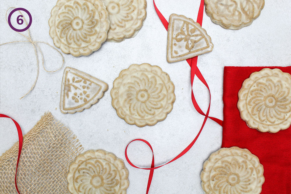 Brown sugar cookies with a flower decoration against a white back drop with red ribbon intertwining the cookies. The image is labeled "6" in the upper left corner.