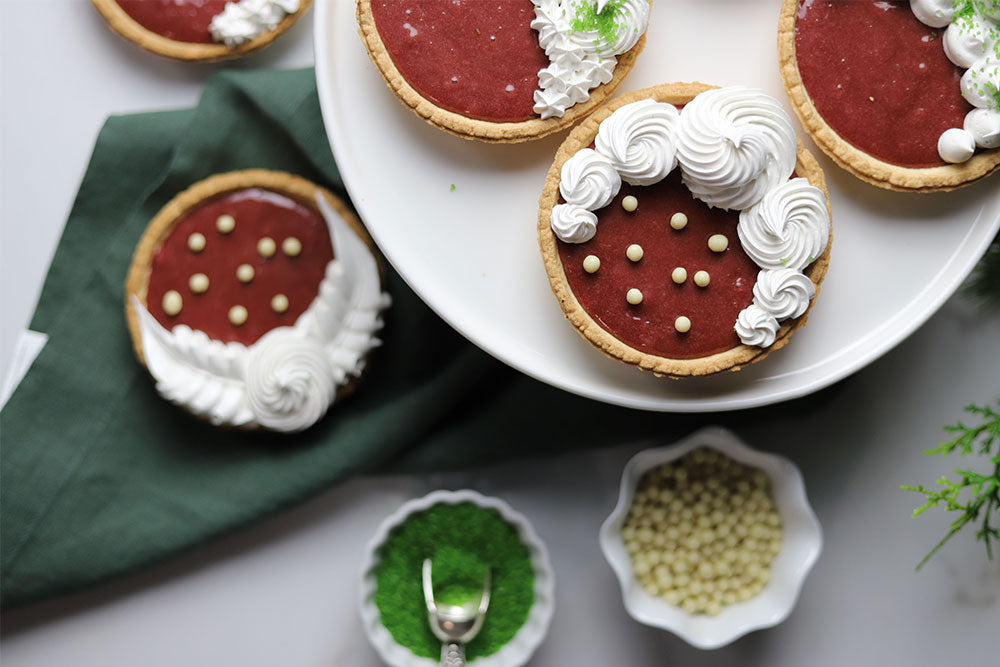 Image of Cranberry Curd Meringue Tarts surrounded by chocolate and sugar décor