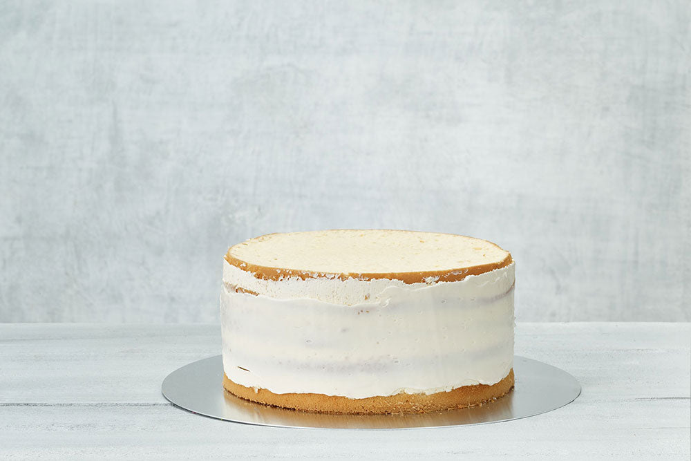 A vanilla cake against a gray backdrop with a crumb-coat of buttercream across the center of the cake. 