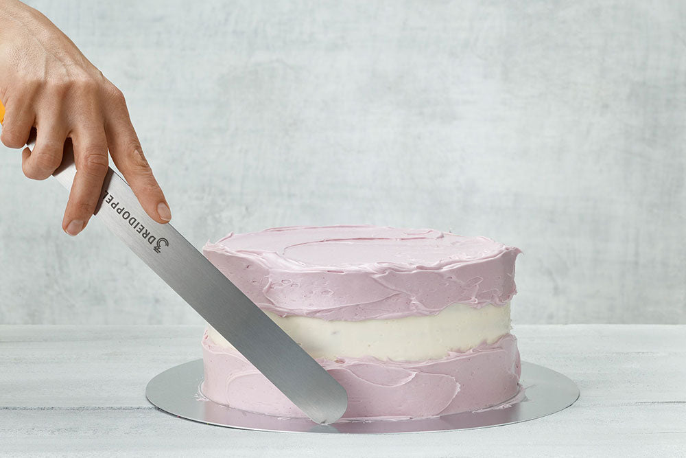 A cake being frosted on the top and bottom with purple frosting against a gray backdrop. 