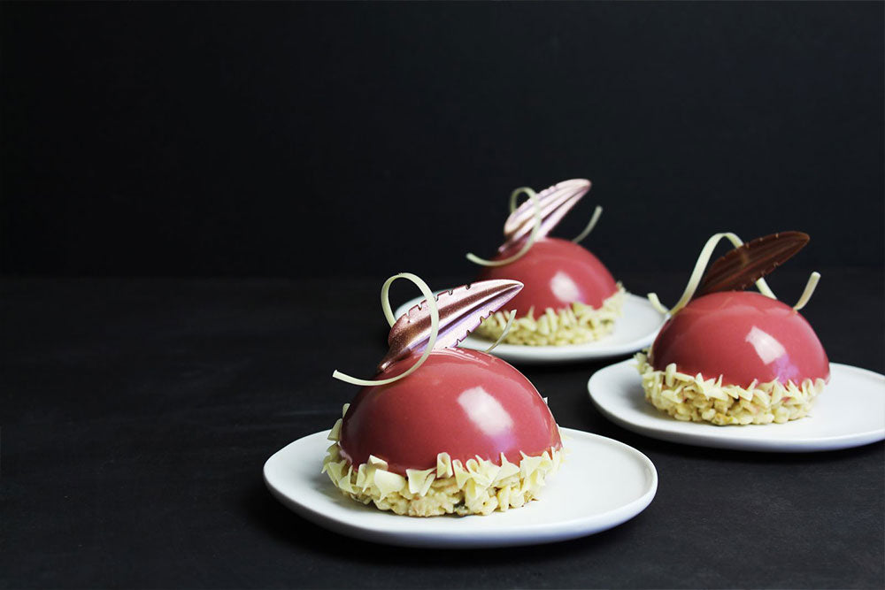 Three Hibiscus entremets with white chocolate decor against a dark backdrop. 