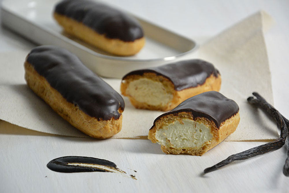 Chocolate Dipped Eclairs on a table, one cut in half to display the cream filling