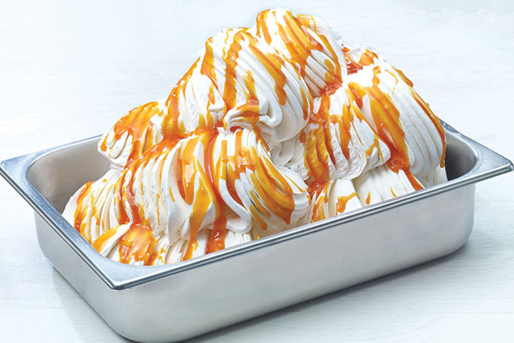 A metal tub filled with a white gelato covered in a caramel sauce. 