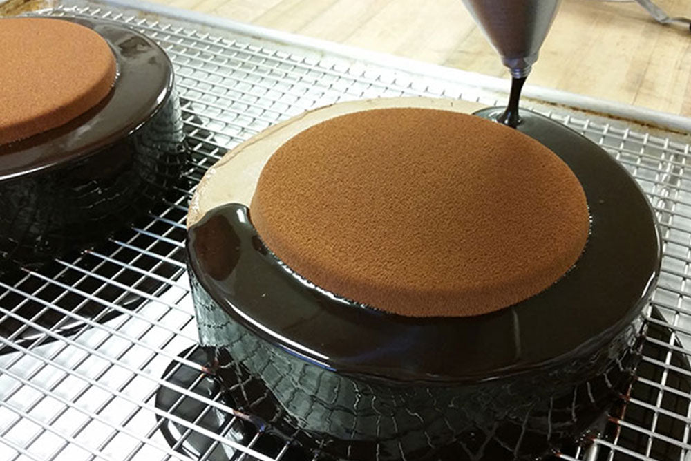 A cake on a drying rack being coated in chocolate ganache. 