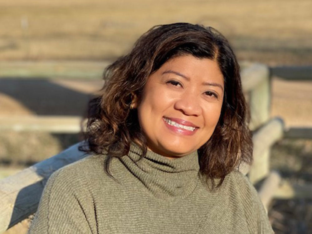 A woman in a gray turtleneck outside near a fence. 