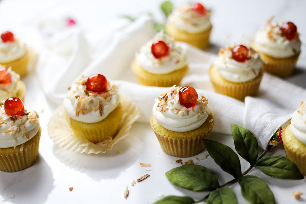 Image of Piña Colada Cupcakes garnished with sweetened coconut flakes and red cherry berries.