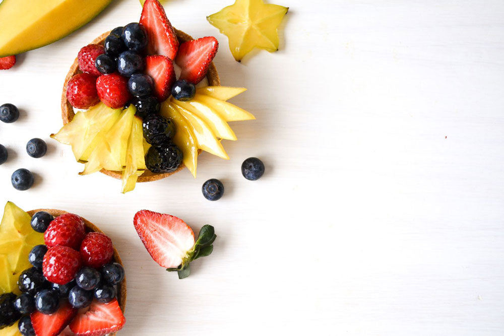 Fruit tarts with a shiny glaze against a gray backdrop to the left of the image. 