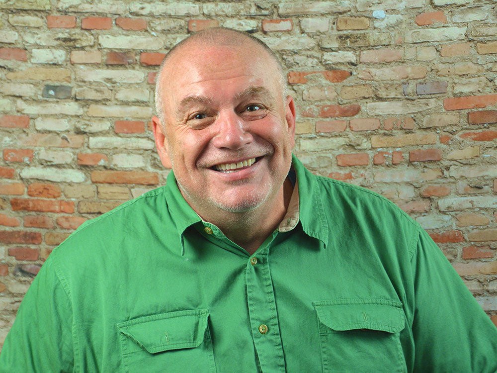 Man in a green shirt in front of a brick wall