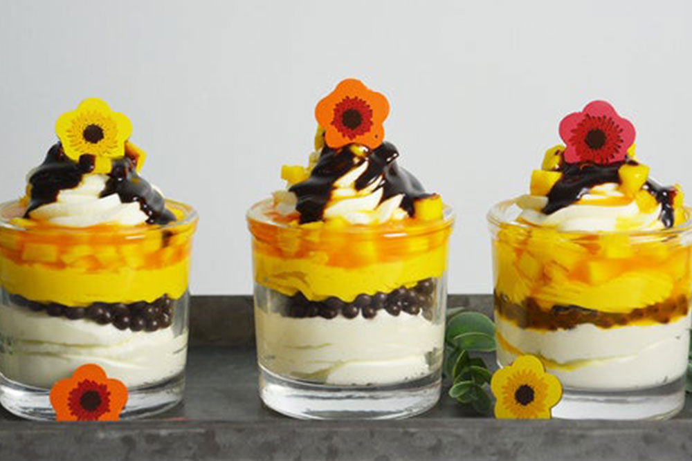 3 Parfaits layered with mousse, passionfruit, and mango with decorative flowers on top 