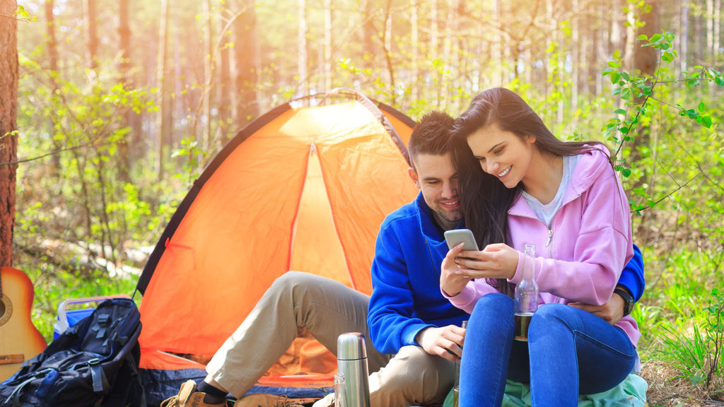 Couple looking up tour information on their mobile phone while camping in a pretty forest