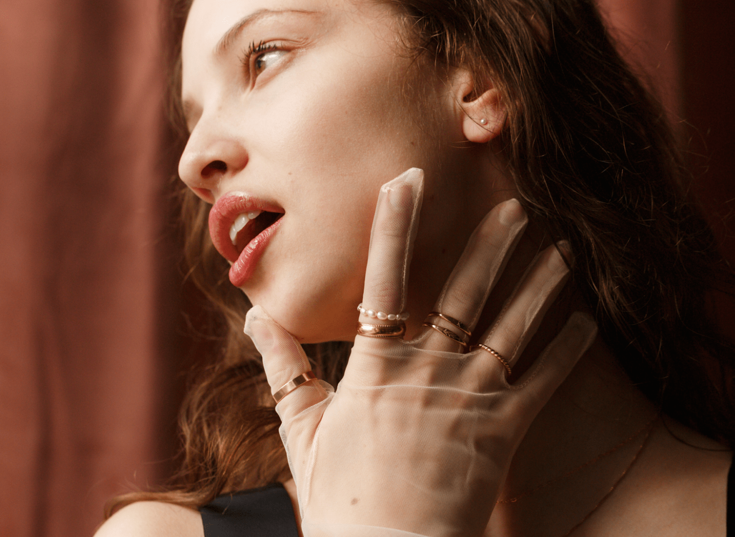 Model wearing various rings of different shapes over sheer gloves