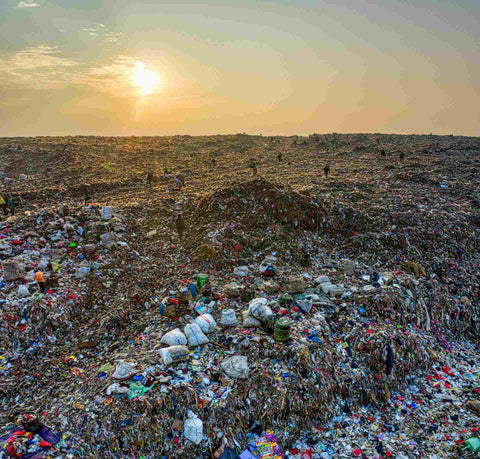 people working at a landfill at sunset. The dump site stretches as far as the eye can see