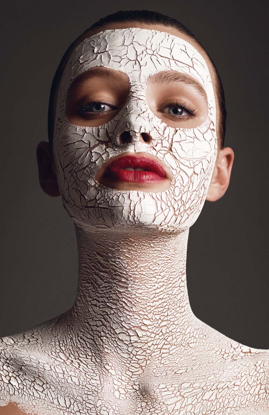 A model with a white face mask applied but with fully made up red lips and eyes