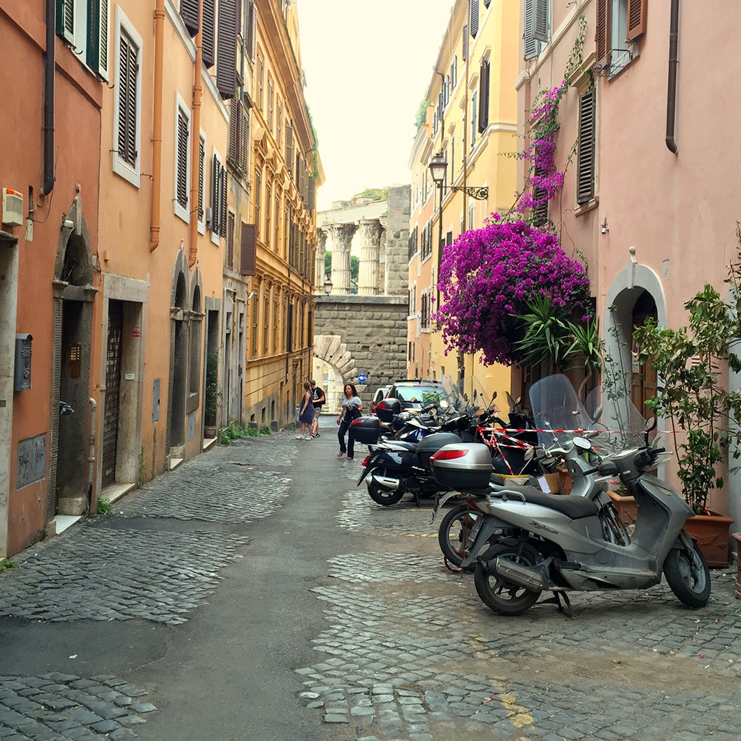 View of Via Baccina's cobblestone street lined with scooters.