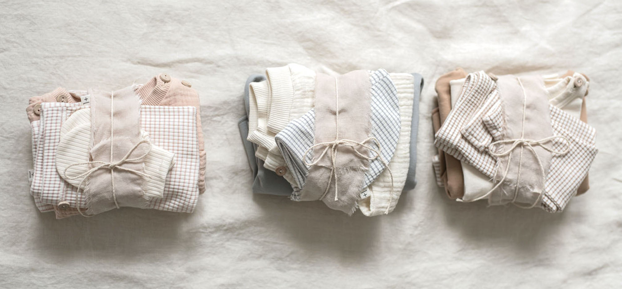 3 bundles of baby clothing tied with string. Natural backdrop