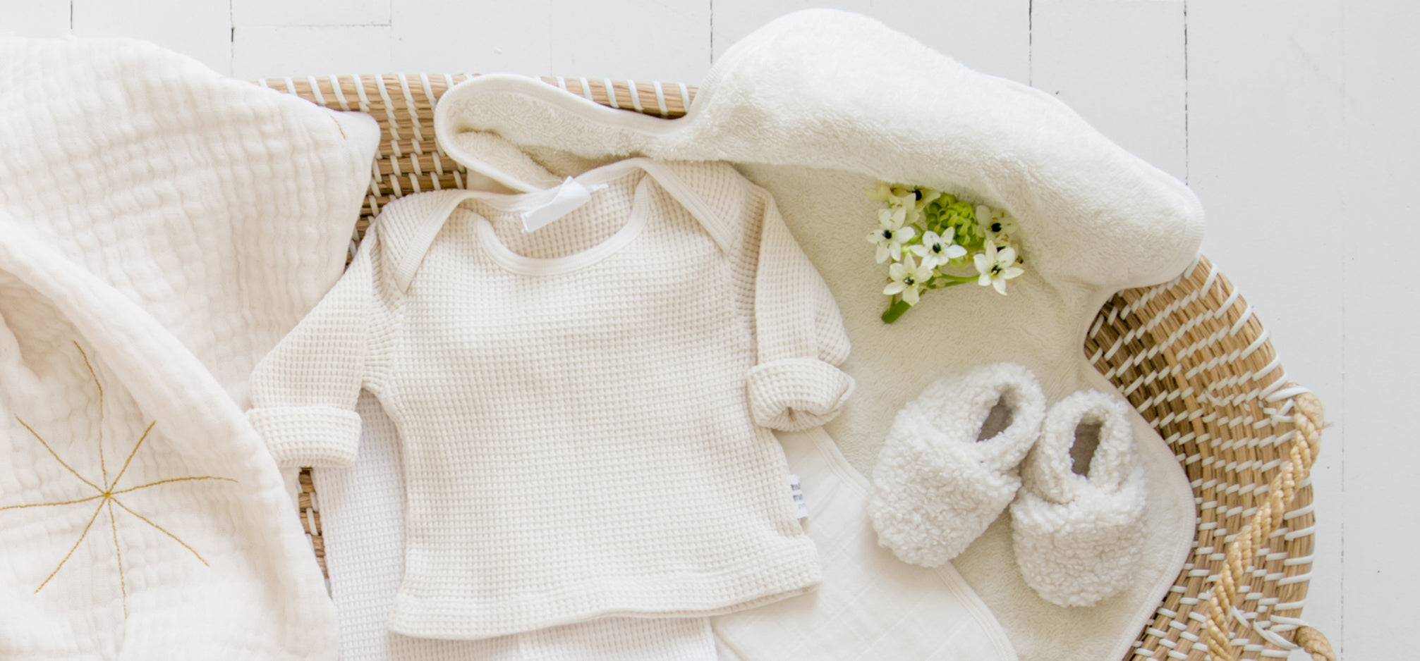 A cream baby outfit and blanket in a seagrass basket.
