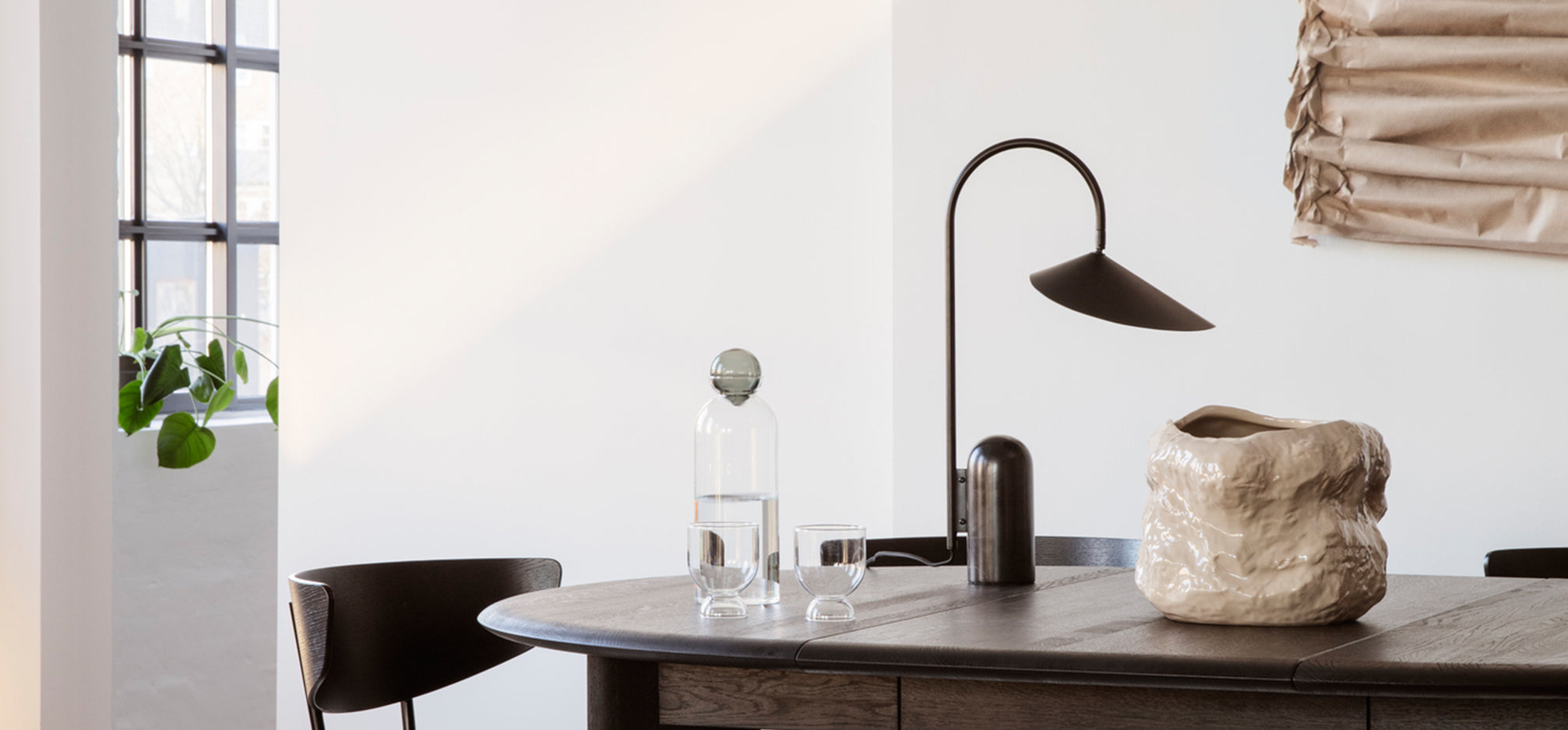 A dining table with a pitcher, lamp and vase on top.