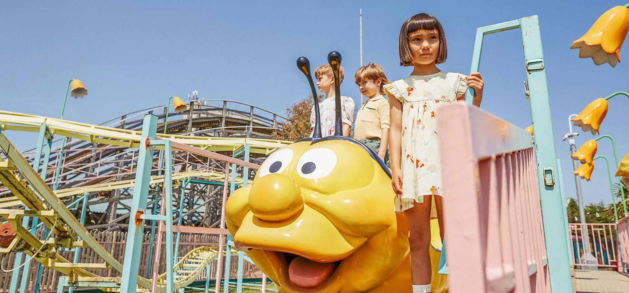 Children at a theme park standing by a ride, wearing morley kids collection SS24