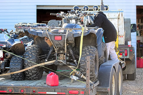 image of hauler tying ATV four-wheelers down to a flatbed trailer using ratchet straps