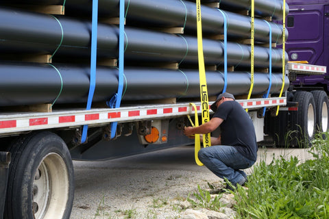 trucker threading strap through flatbed trailer winch for cargo securement