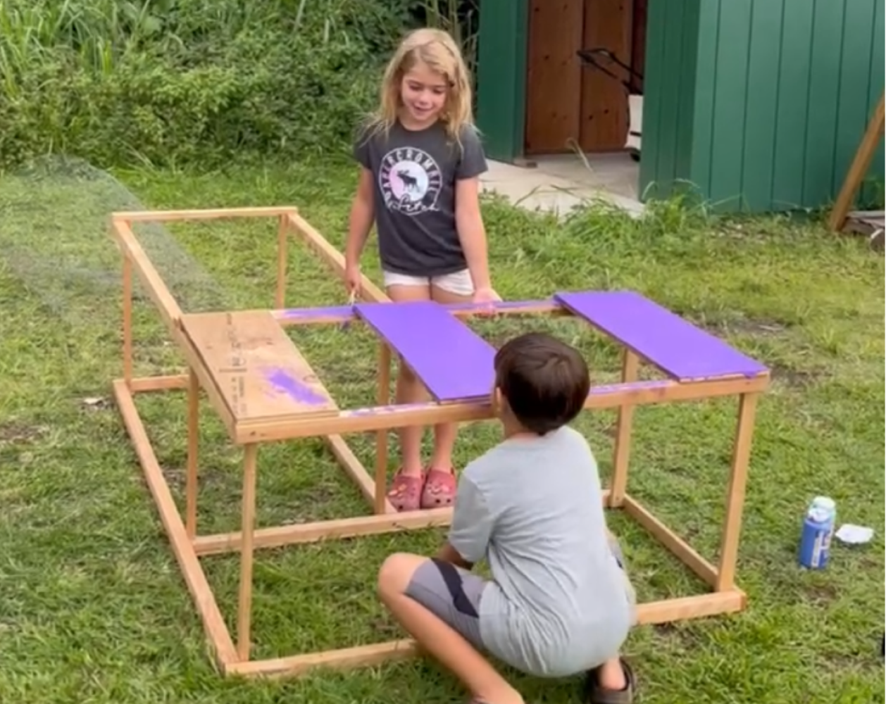 Two children assembling a wooden table outdoors.
