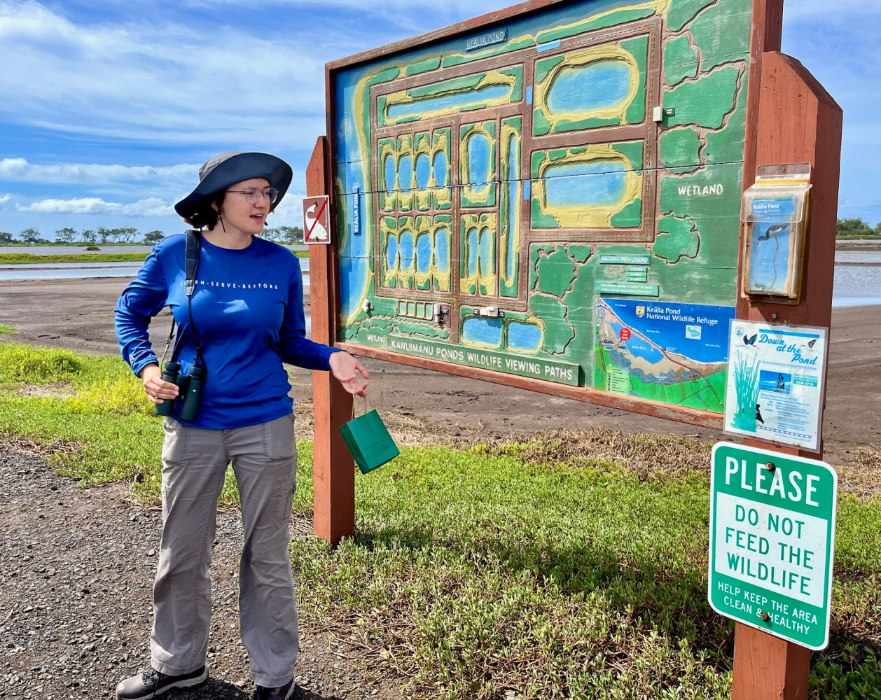 Woman standing next to a park map sign with a 'Do Not Feed Wildlife' notice.