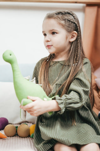 Girl in a green dress holding a stuffed green dinosaur