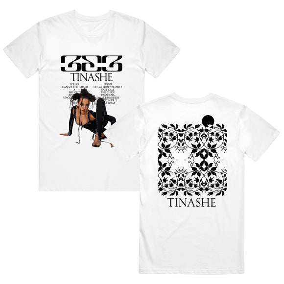 Image of the front and back of a white tshirt against a white background. The front of the tee in black text across the chest reads 333. below that says tinashe. below that in small black text is the track listing to the album 333. There is an image of tinashe posing in a black outfit on the ground against the white color of the tshirt. the back of the shirt features a pixelated abstract flowery design in black and in the shape of a square. Below this in black text reads 