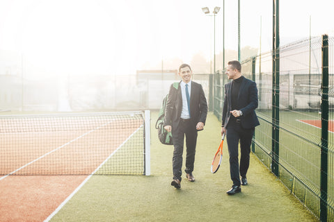 Two people with tennis racquet bags on a tennis court