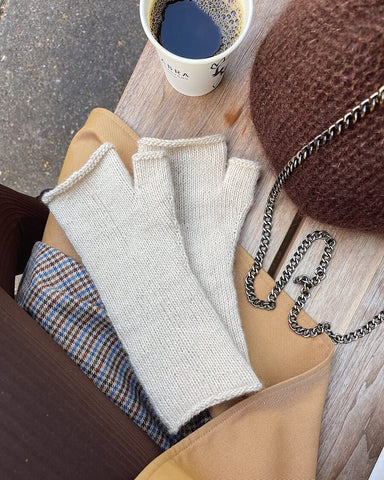 fingerless mitts laying on a table next to a cup of coffee