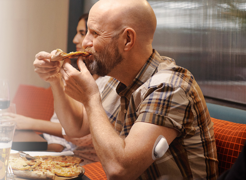 Man eating pizza showing Omnipod 5 on upper arm