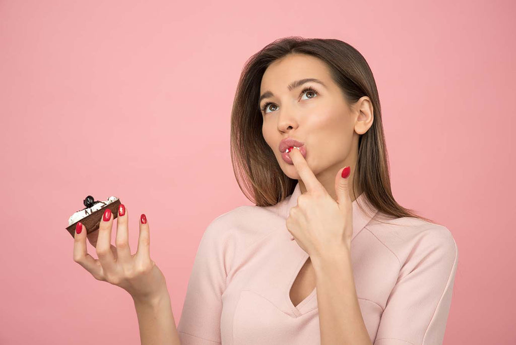 Female looking thoughtful holding chocolate cake and licking finger.