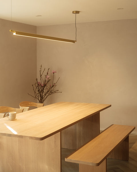 Wooden scandi dining interior with minimalist linear pendant Ando chandelier in brass turned on