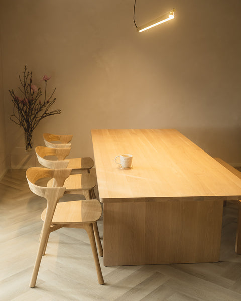 Wooden scandi dining interior with minimalist linear pendant Ando chandelier in brass turned on