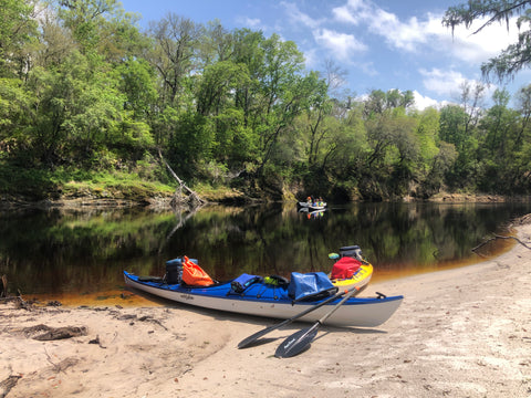 Kayaks on a riverside beach with camping gear