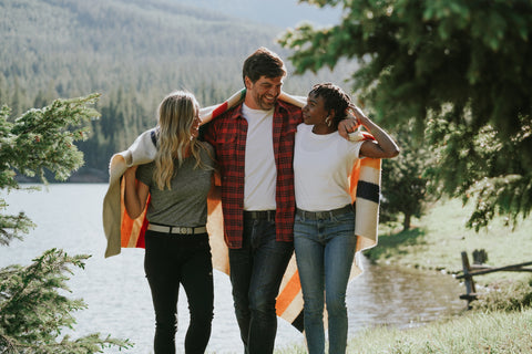 A group of friends all wearing Jelt belts and wrapped in a Pendleton blanket walking in front of a mountain lake 