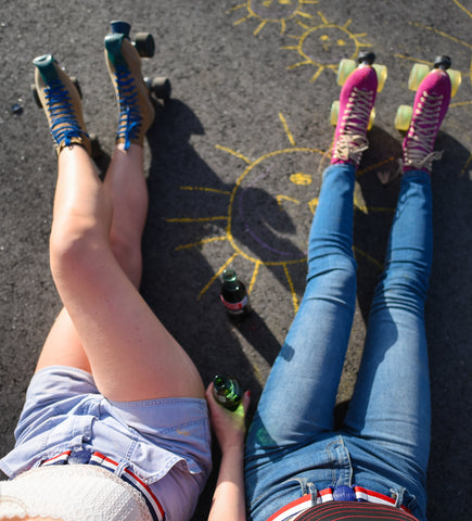 Girls wearing roller skates, sitting on pavement. Wearing Jelt USA Stripe Elastic stretch belts with their summertime look.