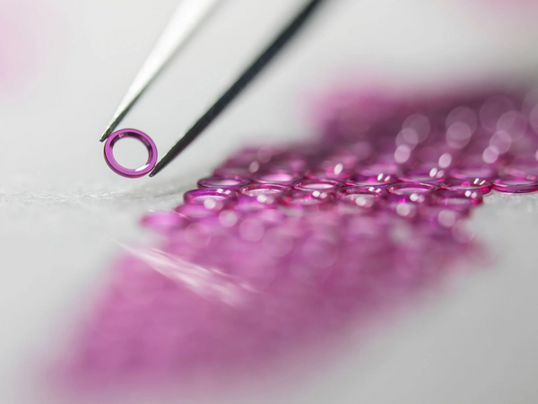 un bijou de montre, un anneau rose violet tenu par une pince et des bijoux en dessous 