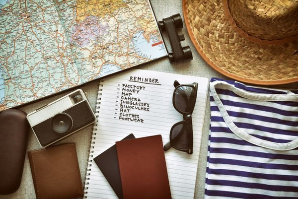 Zoom sur des accessoires de voyage ; lunette, tee-shirt, chapeau, carnet, appareil photo, carte du monde