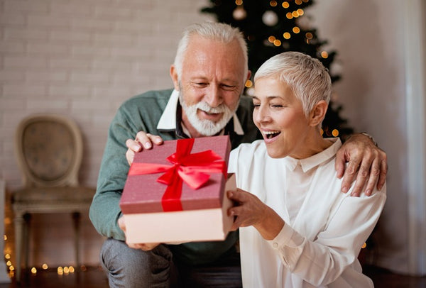 Un homme et une femme, le visage heureux, ouvrant une boite-cadeau au ruban rouge