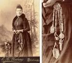 Ancienne photographie s'une femme portant une montre à gousset avec une chatelaine, présentation de la chatelaine à droite avec plusieurs chaines reliées à des petits objets