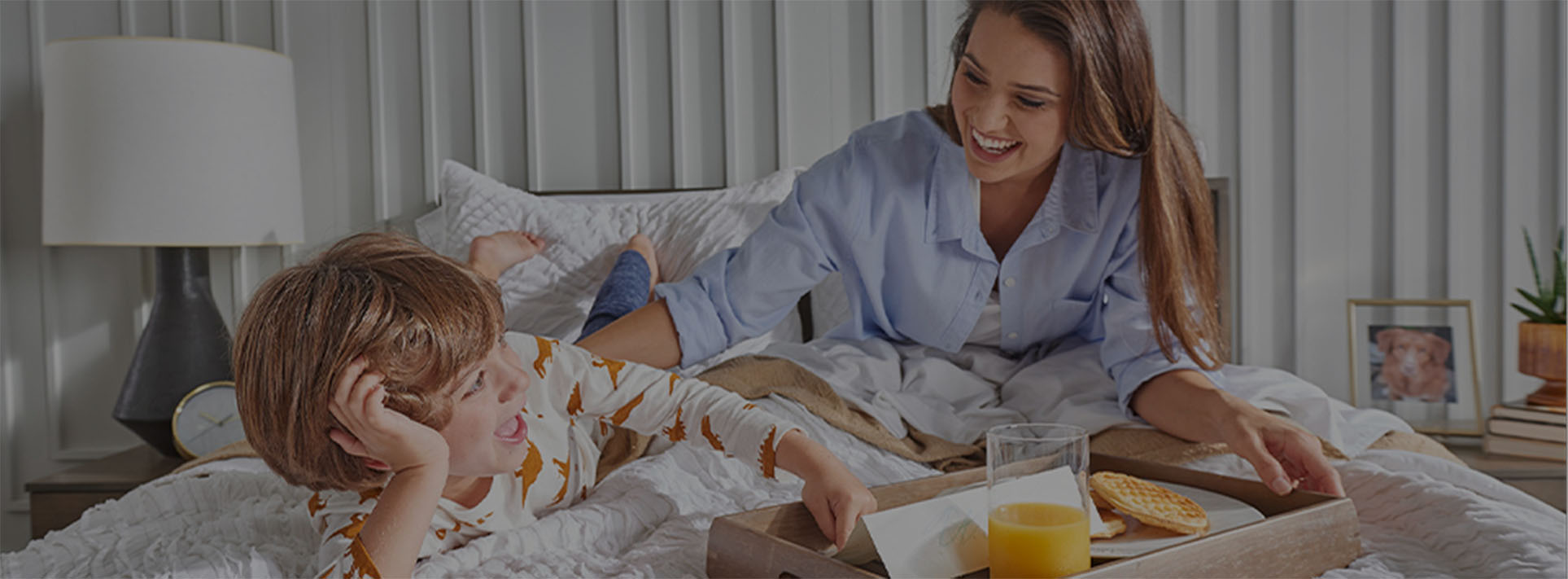 Mom and son eating breakfast in bed on a Sealy® bed