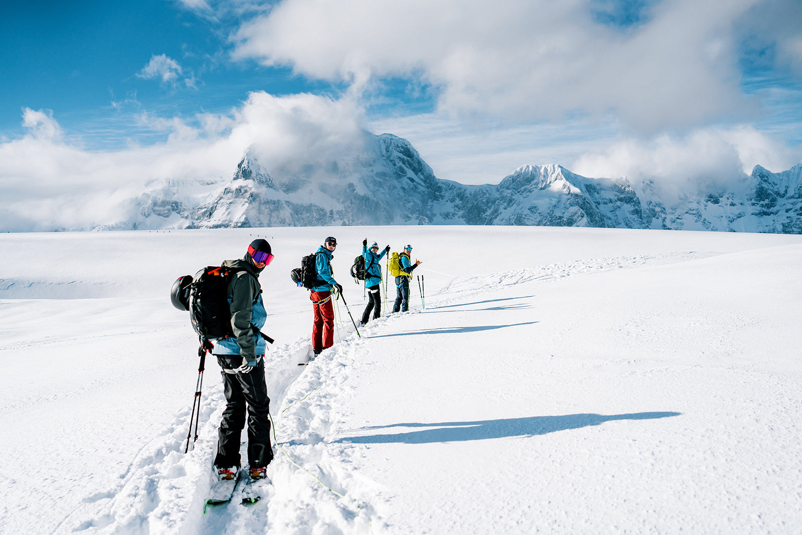 Four skiers in a skin track with cloudy snowy mountain backdrop